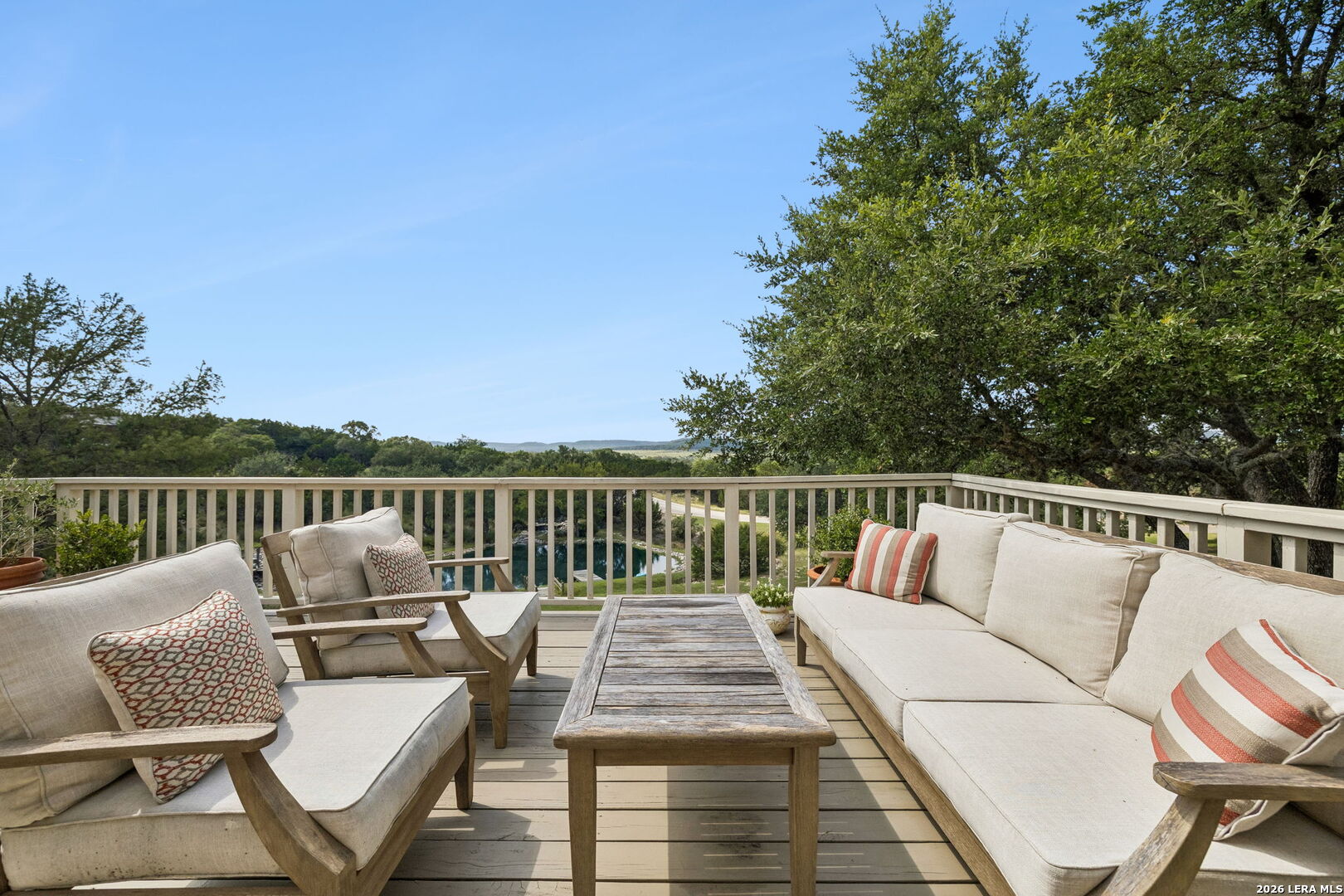 Furnished outdoor deck with cushioned seating, a wood coffee table, and wooded views with a glimpse of water.