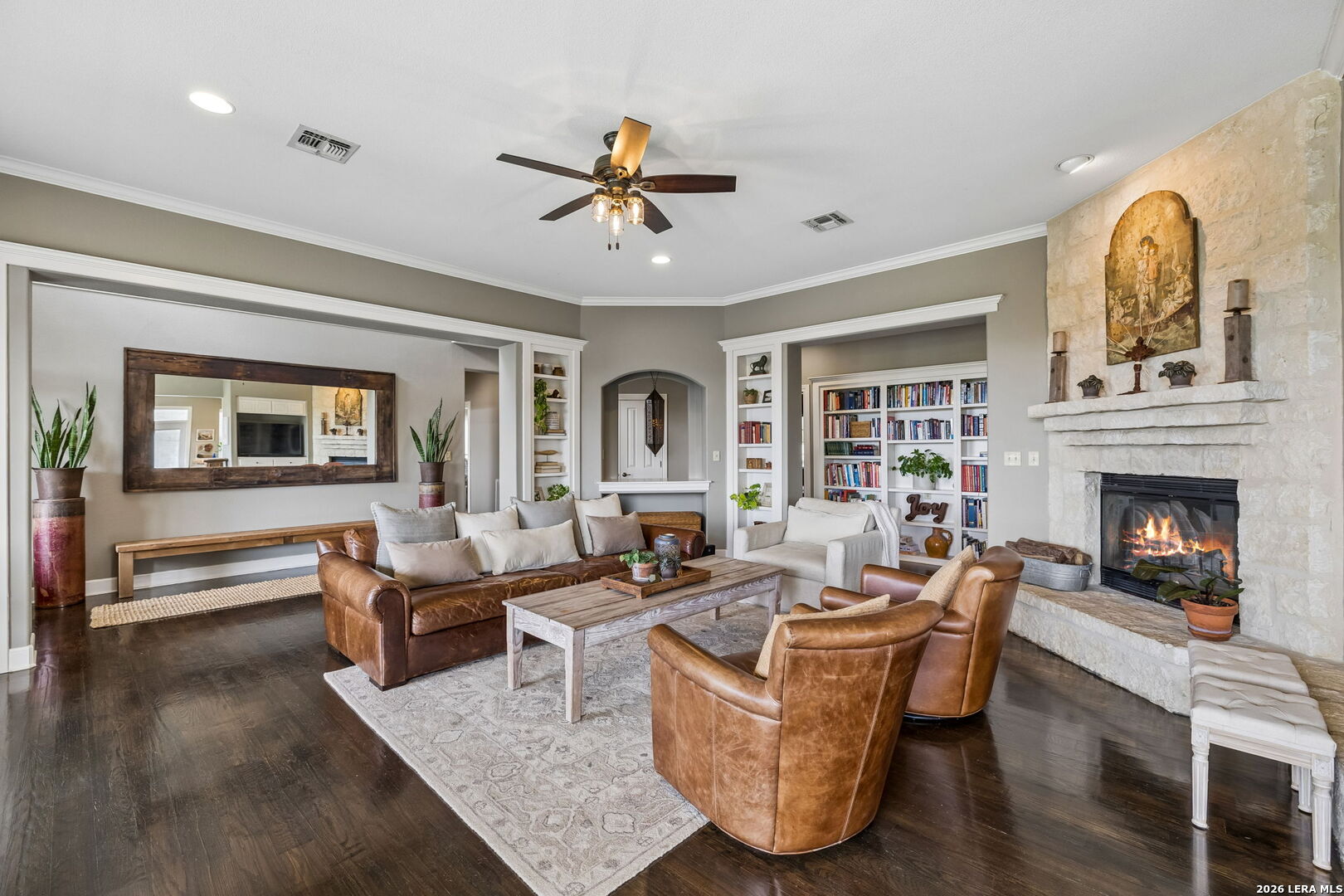 Living room with a stone fireplace, leather seating, built-in bookshelves, and dark wood floors.