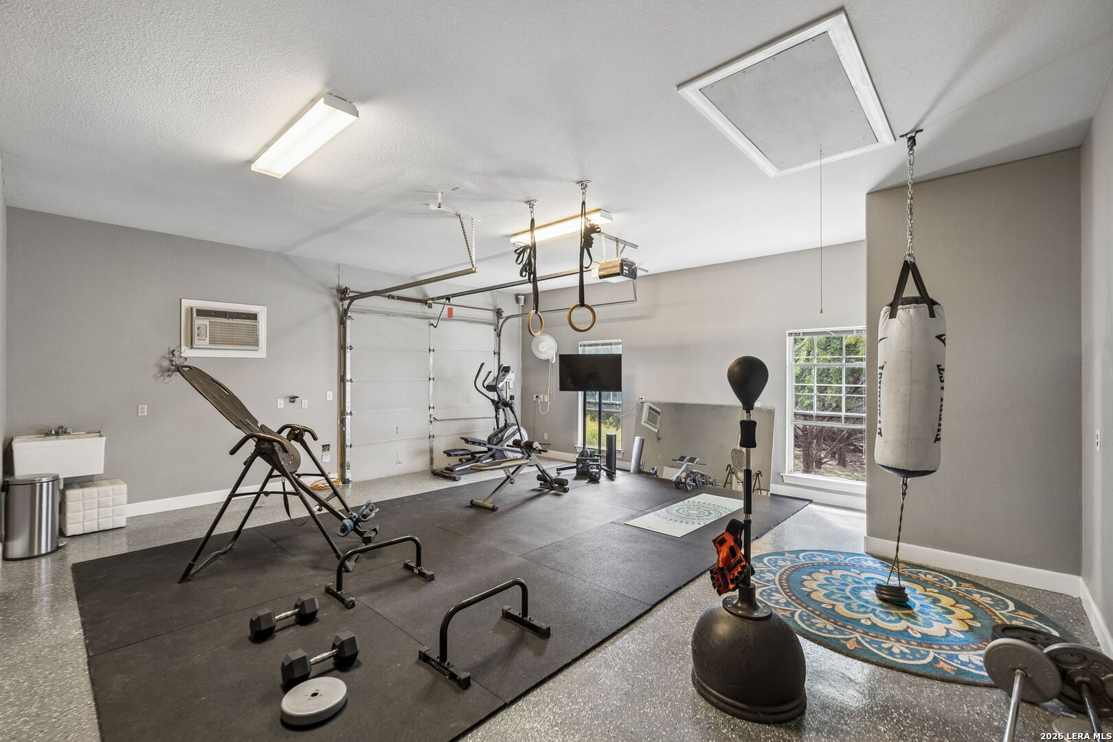 Garage gym with rubber flooring, exercise equipment, gymnastic rings, and a hanging punching bag.