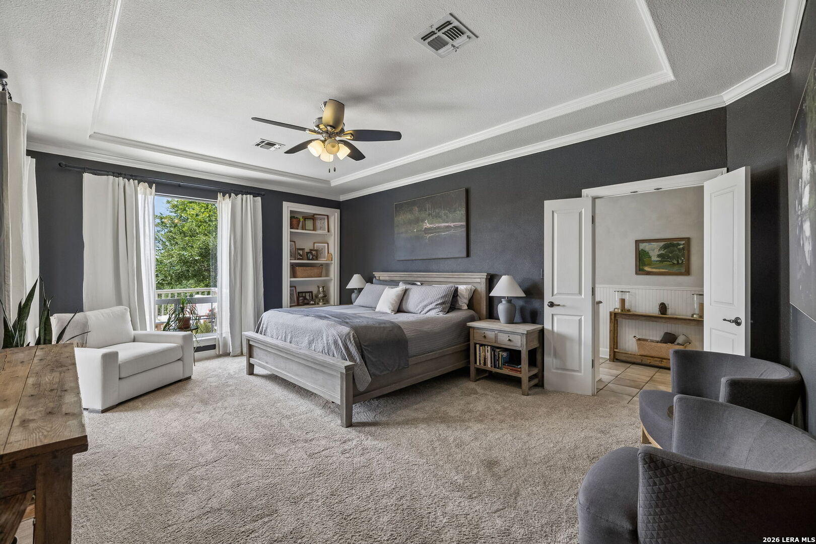 Bedroom with a large gray bed, dark walls, a sitting area, and open doors to a tiled room.