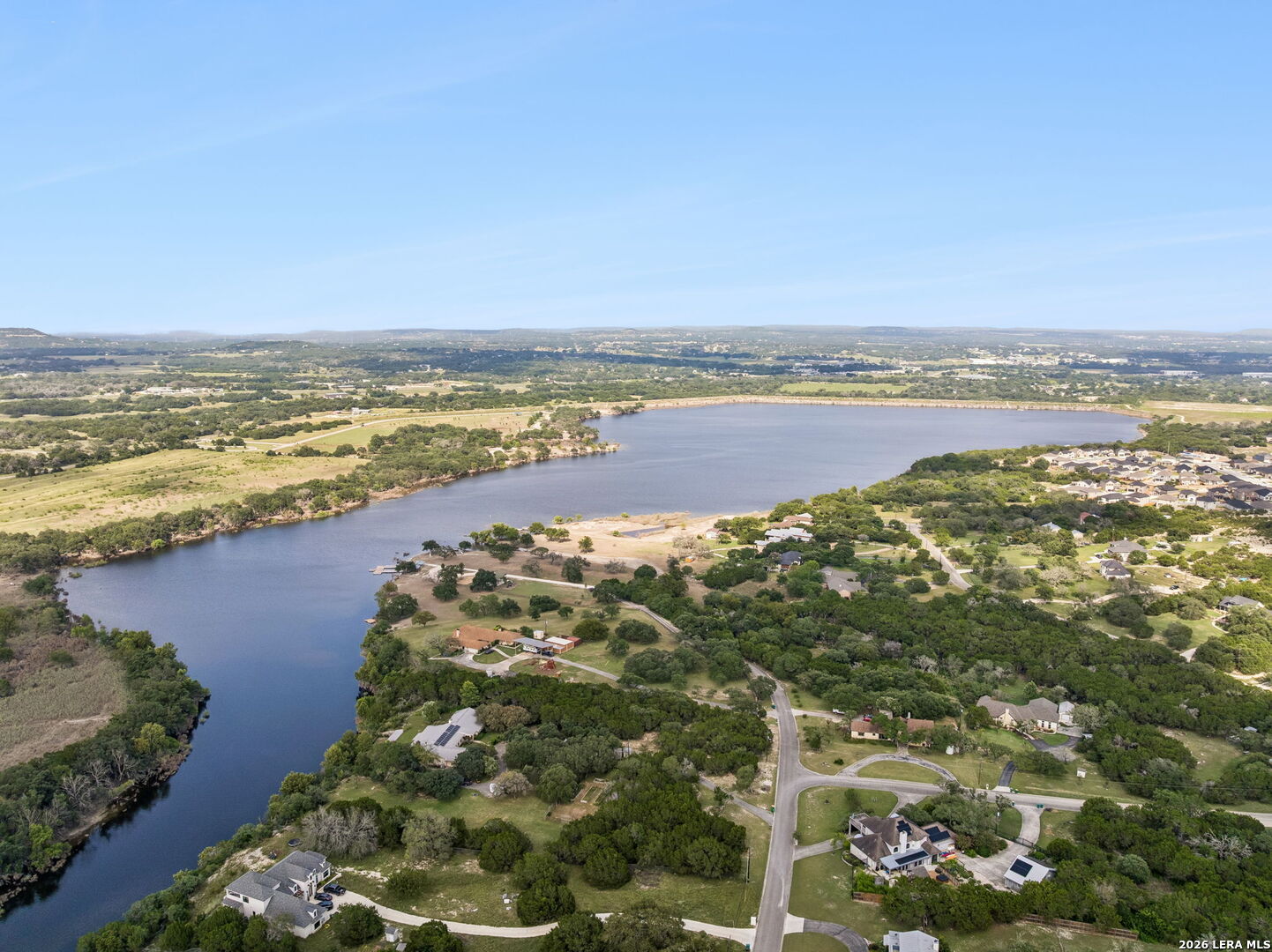 Aerial view of a lake, with wooded shores, nearby homes, and a residential neighborhood.
