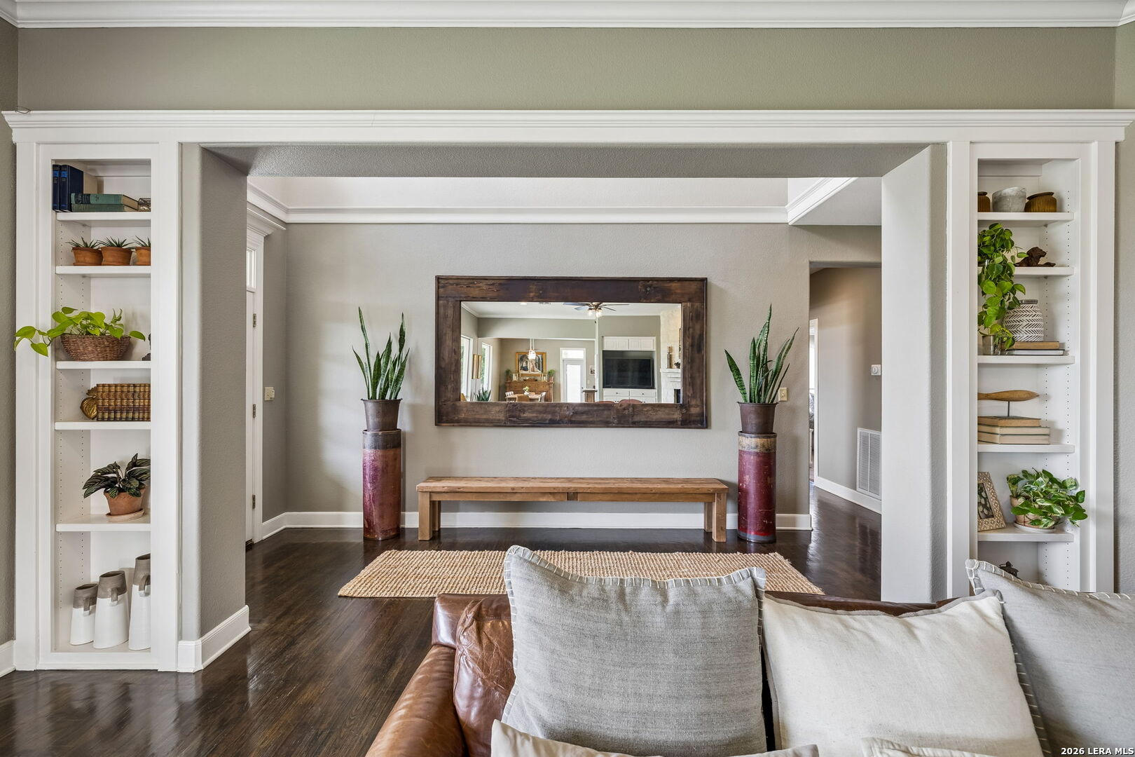 Living room with built-in display shelves, a large mirror, wooden bench, and leather sofa.
