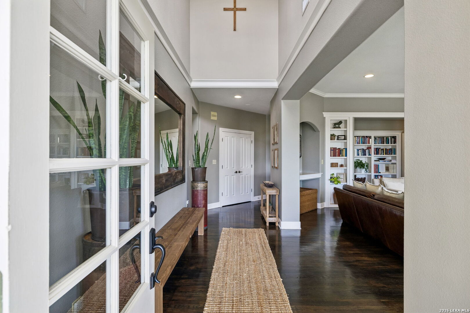 Entry hall with a high ceiling, dark hardwood floors, woven runner, and view into a living room with built-in bookshelves.