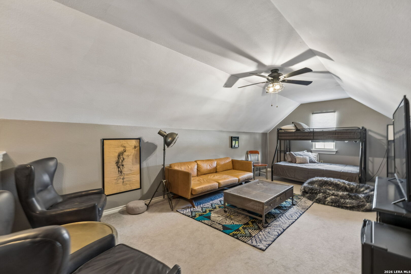Furnished loft with a metal bunk bed, tan leather sofa, and seating area beneath a vaulted ceiling.