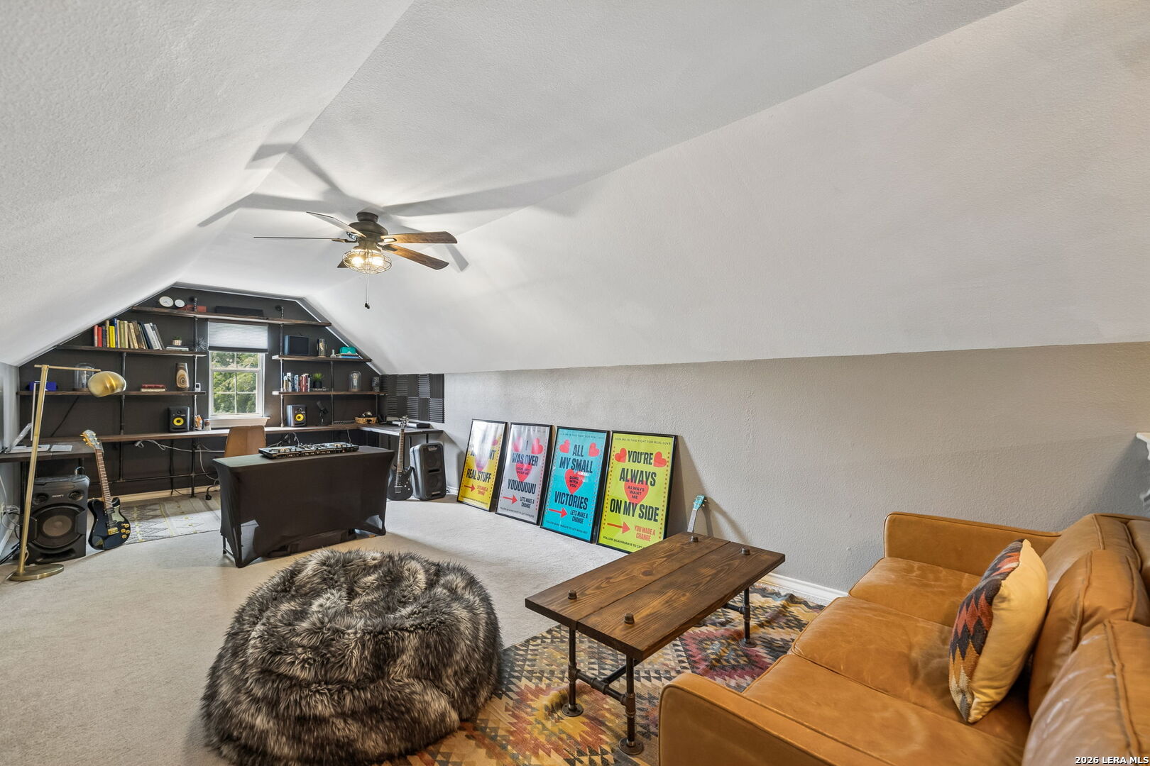 Furnished attic music room with a sloped ceiling, built-in shelves, guitars, and a brown leather sofa.