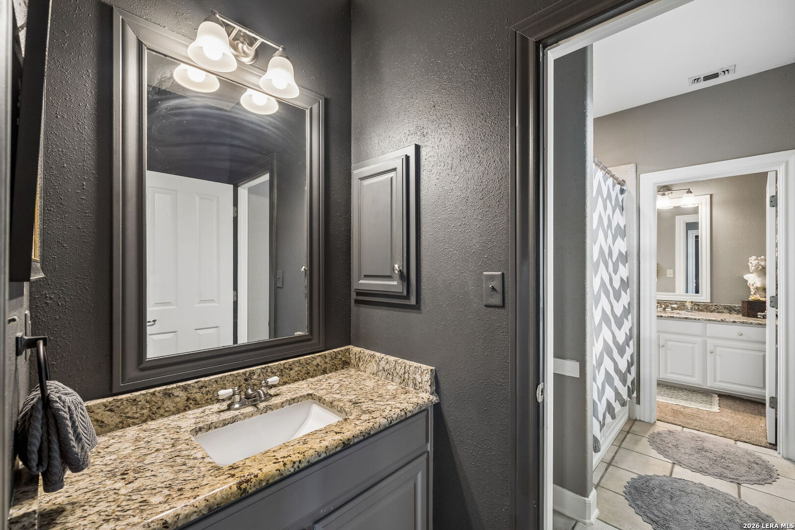 Bathroom with granite vanity, dark walls, large mirror, and adjoining shower area.