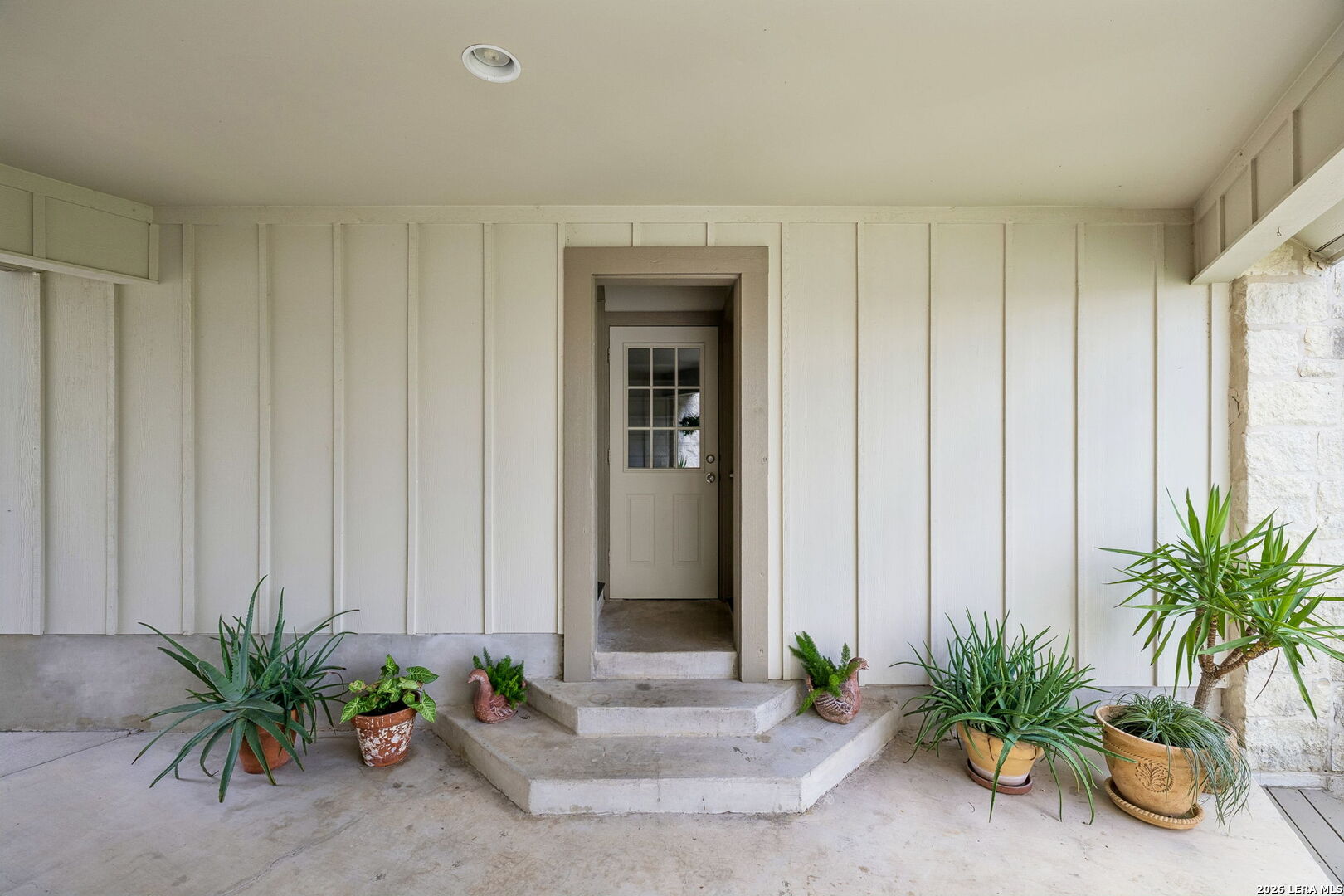 Covered entry with a glass-paneled front door, concrete steps, and potted plants.