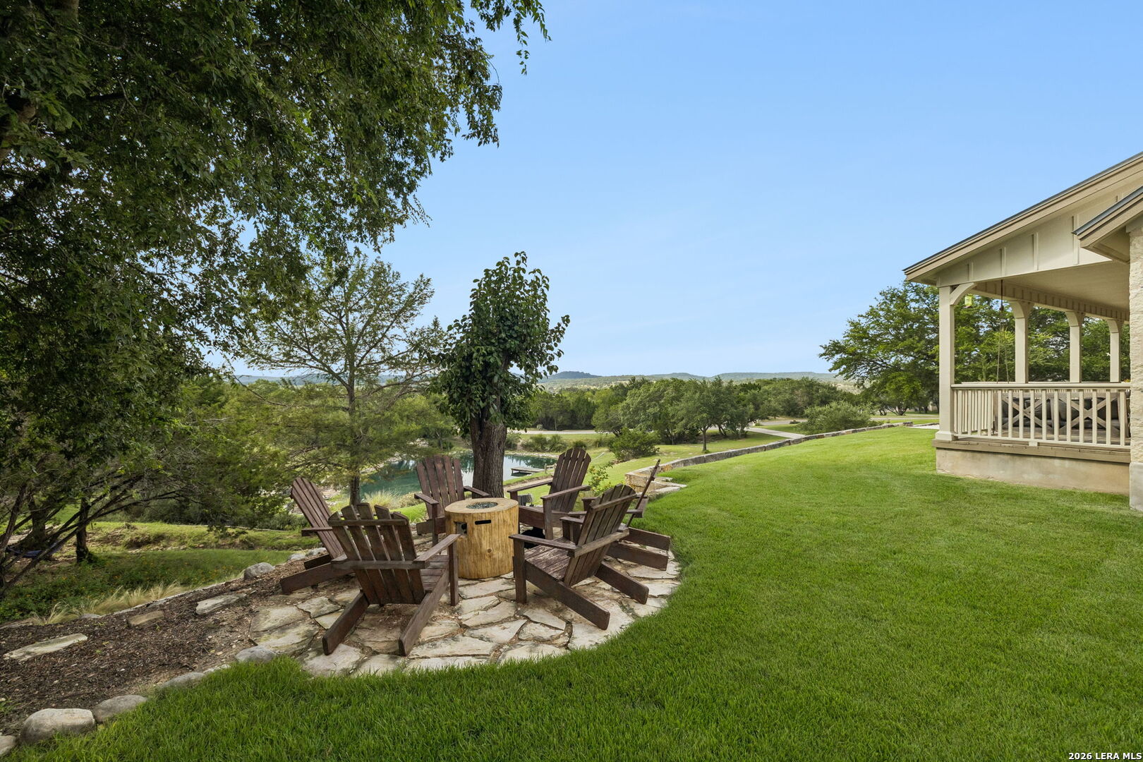 Backyard patio with Adirondack chairs and fire pit overlooking water and wooded hills.