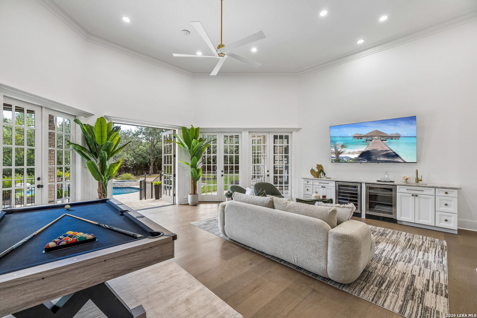 Game room with billiards table and sectional, opening through French doors to a pool.