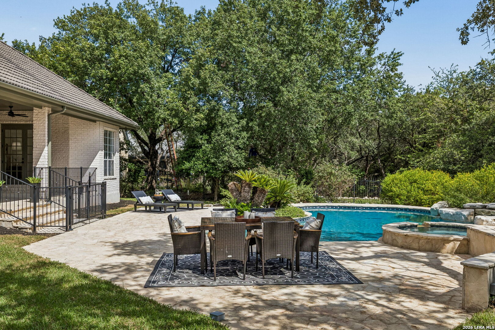 Backyard pool and raised stone spa beside a shaded stone patio with outdoor dining furniture.