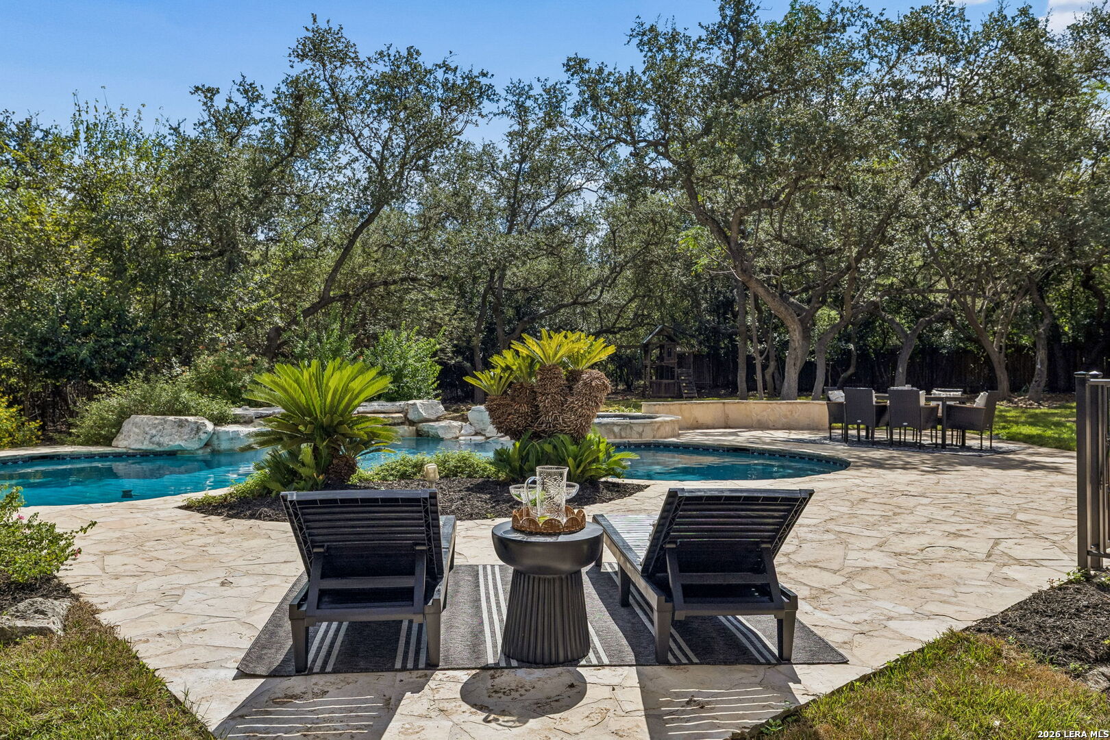 Backyard pool and flagstone patio framed by mature trees, with lounge chairs and outdoor dining furniture.