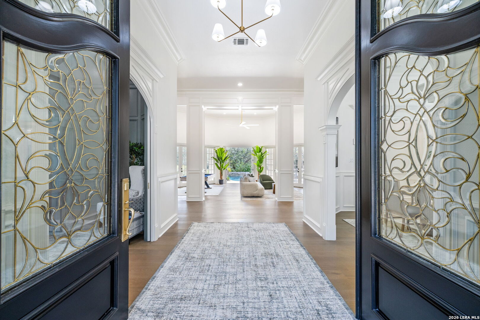 White paneled foyer framed by ornate glass doors, with a long rug leading to a bright living area.