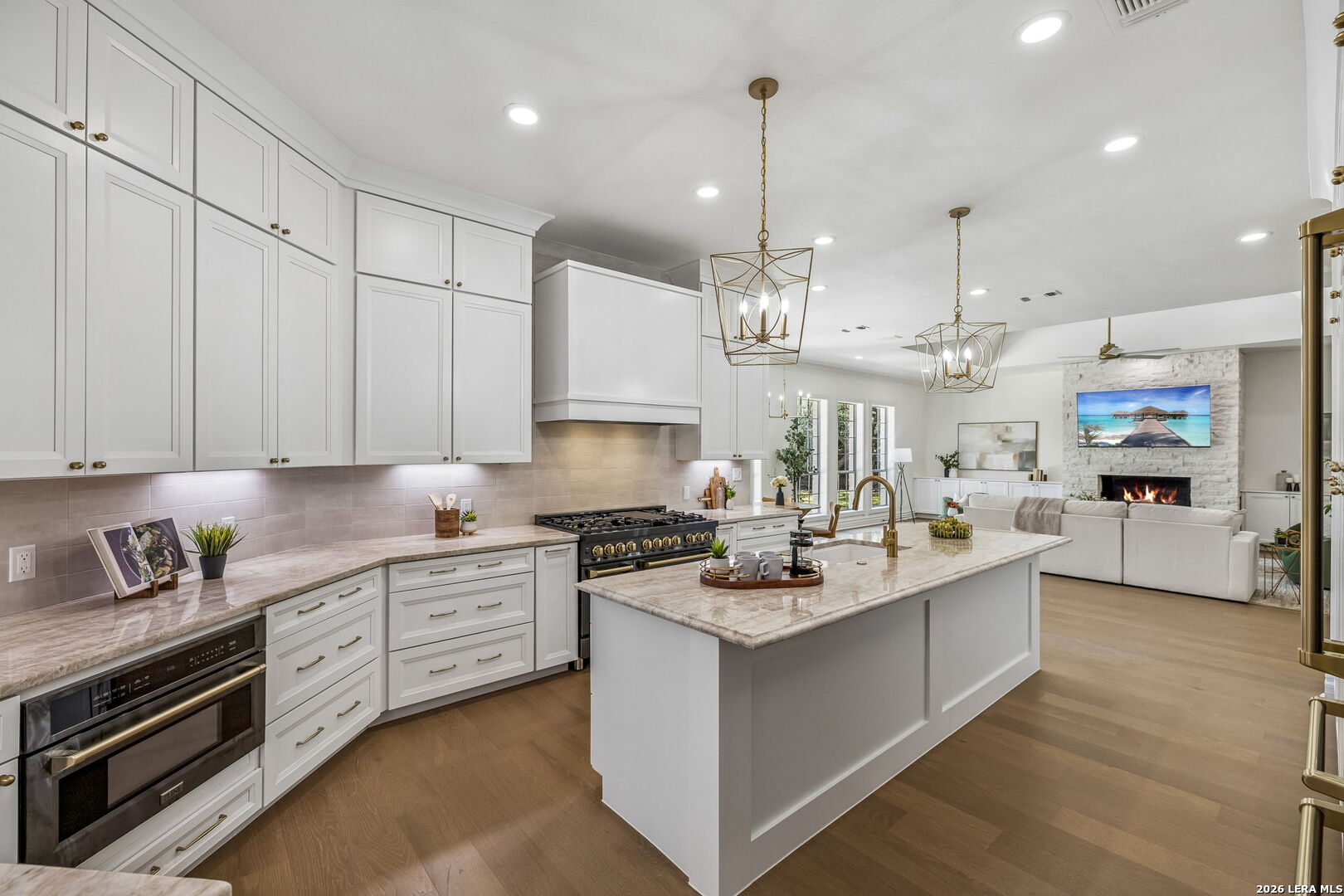 Bright white kitchen with a large stone island, brass fixtures, and an open view to the living room.