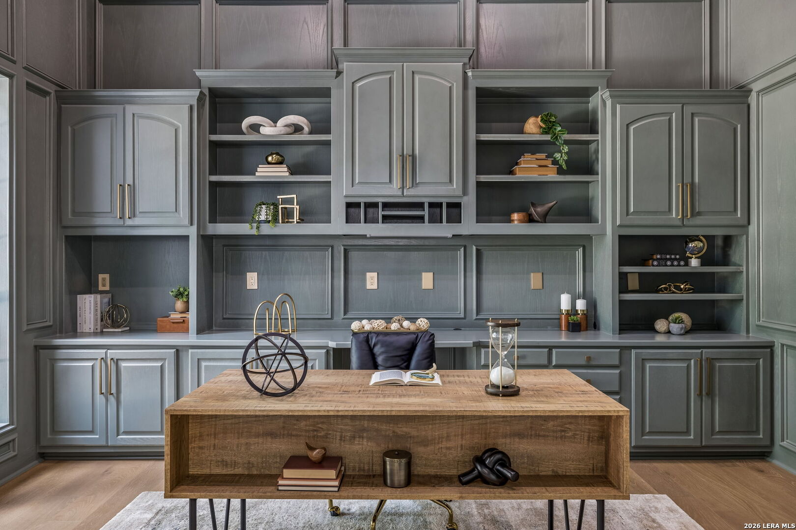 Gray built-in cabinetry and open shelves frame a rustic wood desk in a staged home office.