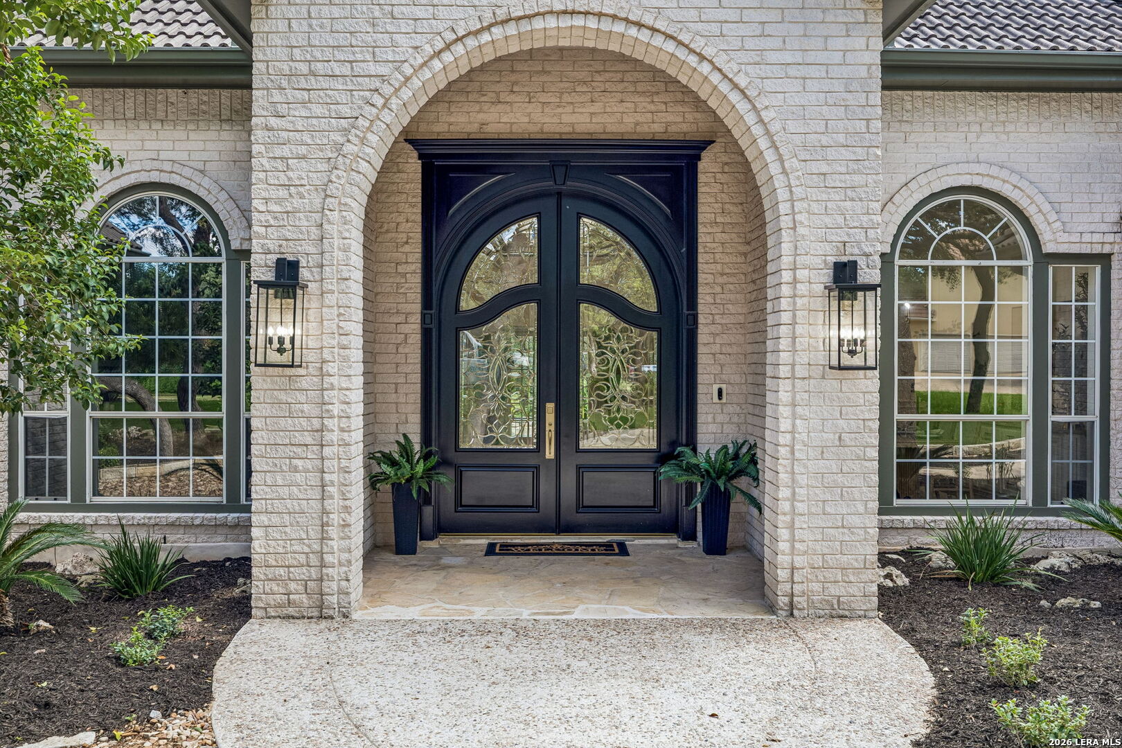 Home entrance with ornate black double doors beneath a broad brick arch, flanked by arched windows.