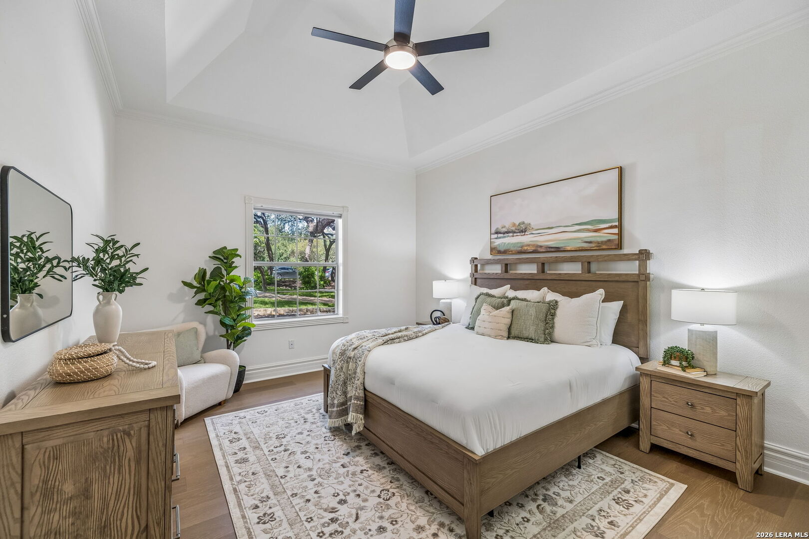 Staged bedroom with a wood bed, patterned rug, and window overlooking trees.