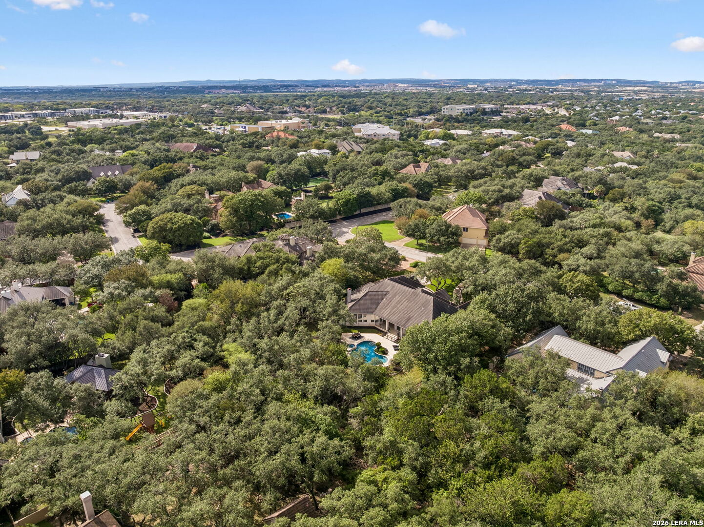 Aerial view of a leafy residential neighborhood with homes, streets, and a backyard pool.