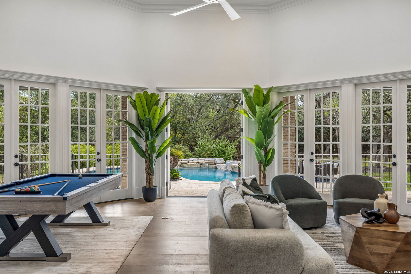 Living and game room with a pool table and seating beside glass doors overlooking a backyard pool.