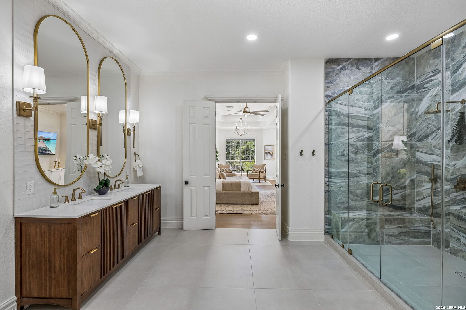 Bathroom with a wood double vanity, arched mirrors, and a marble-look glass shower.