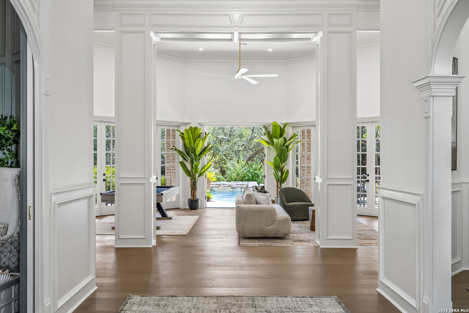 Living room with tall white paneled columns, potted plants, and a view of the backyard pool.