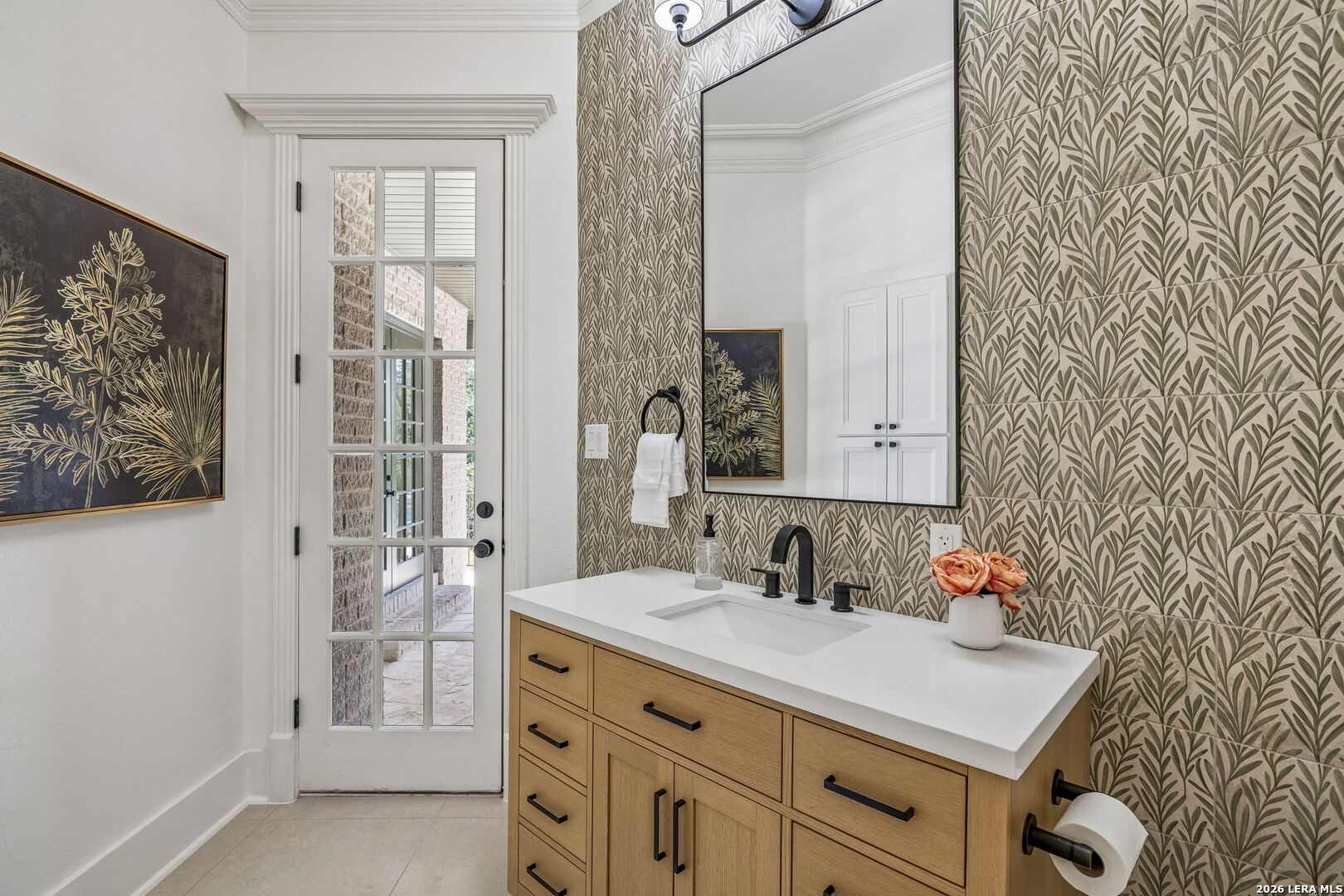 Bathroom vanity with leafy wallpaper, a light wood cabinet, and a glass-paneled door.