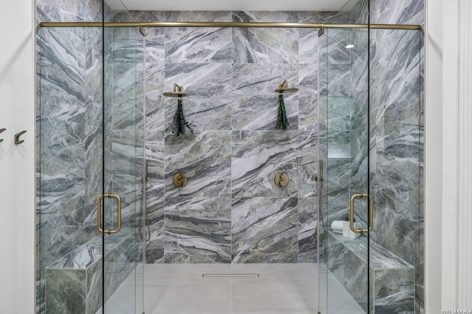 Walk-in shower with dramatic gray veined stone tile, brass fixtures, and built-in benches.