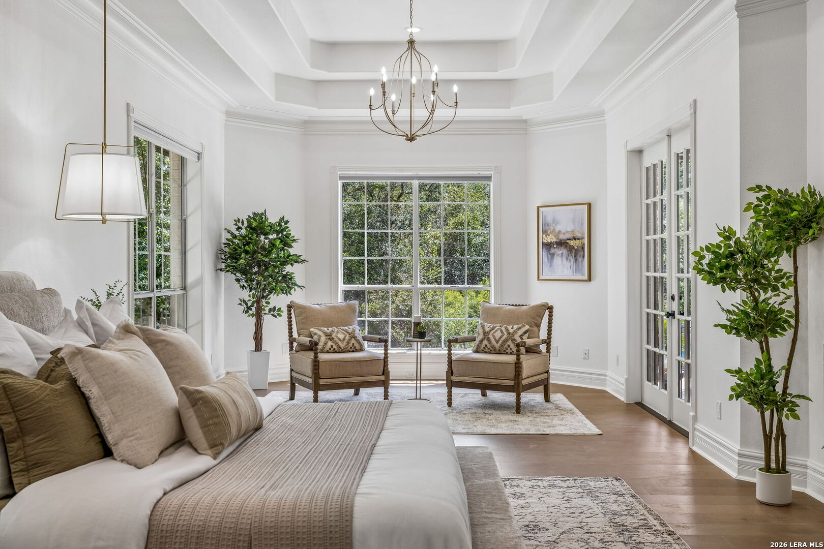 Staged living room with a white sofa, two armchairs, large windows, and French doors.