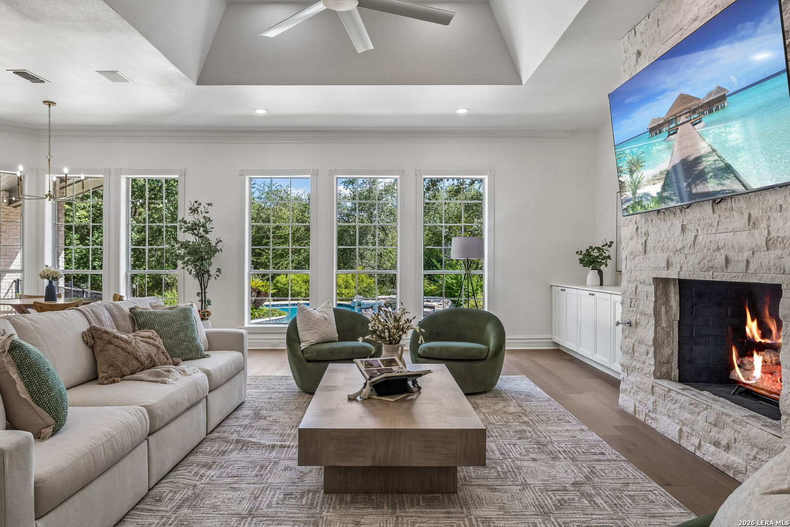Living room with tall pool-view windows, green chairs, and a stone fireplace.