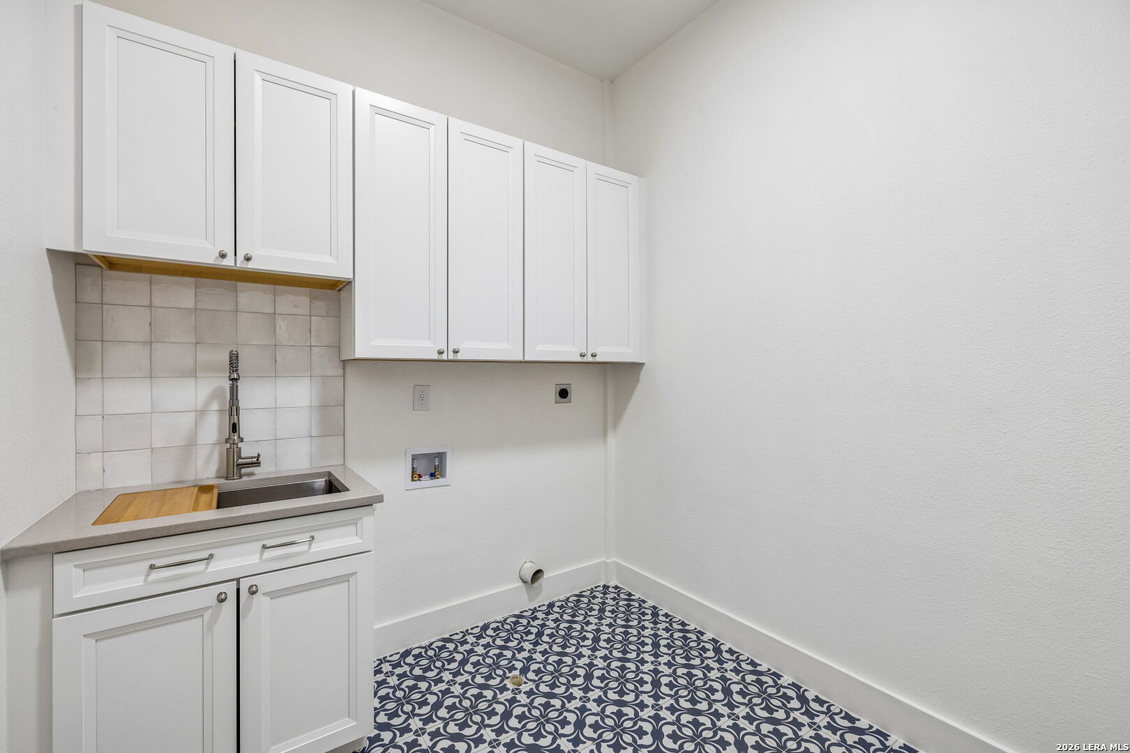 Laundry room with white cabinets, utility sink, washer hookups, and patterned blue-and-white tile floor.