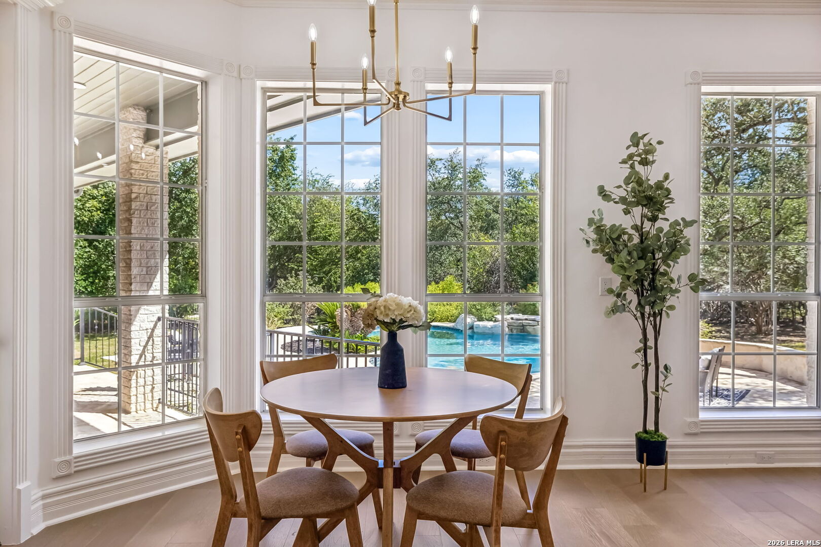 Dining room with a round table and large windows overlooking a backyard pool.