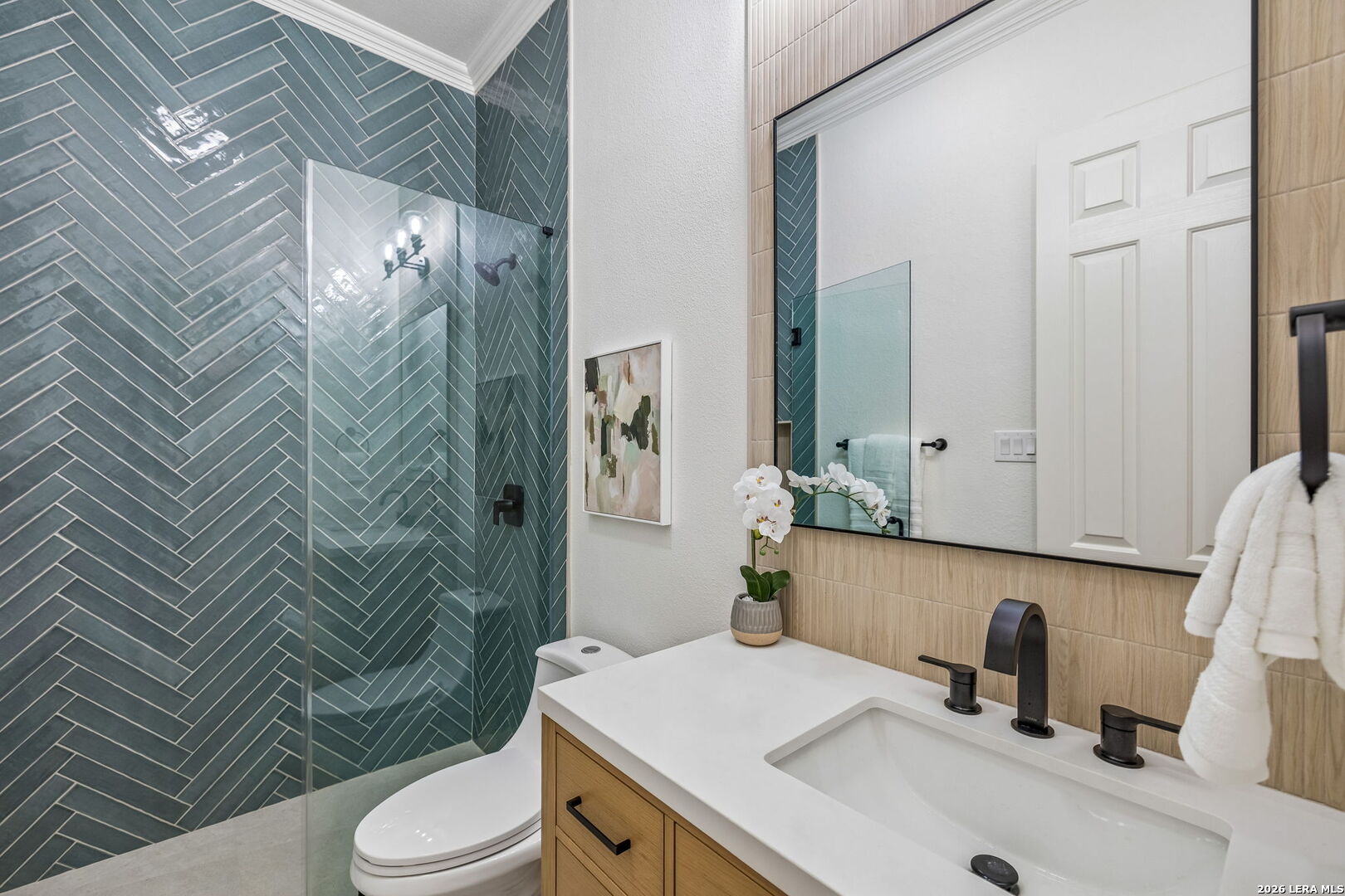 Bathroom with a blue-gray herringbone tile shower and light wood vanity.