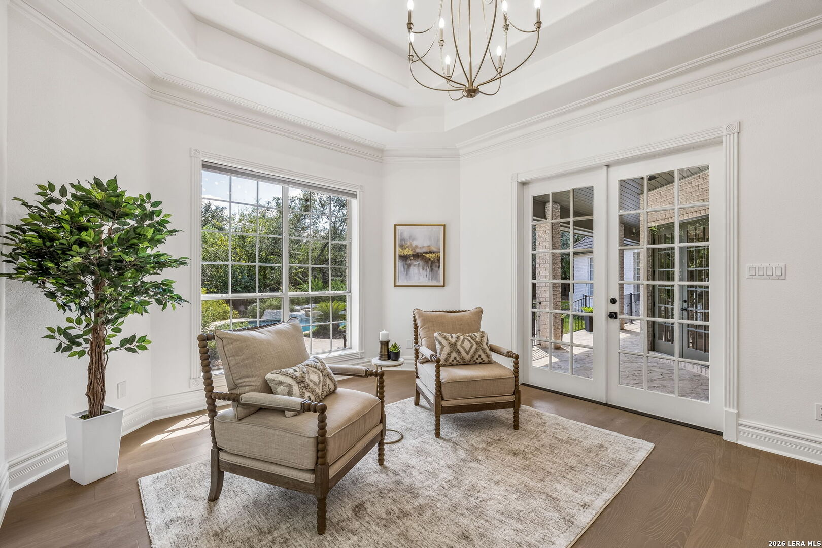 Staged sitting room with two armchairs, a large window, and French doors opening to a patio.
