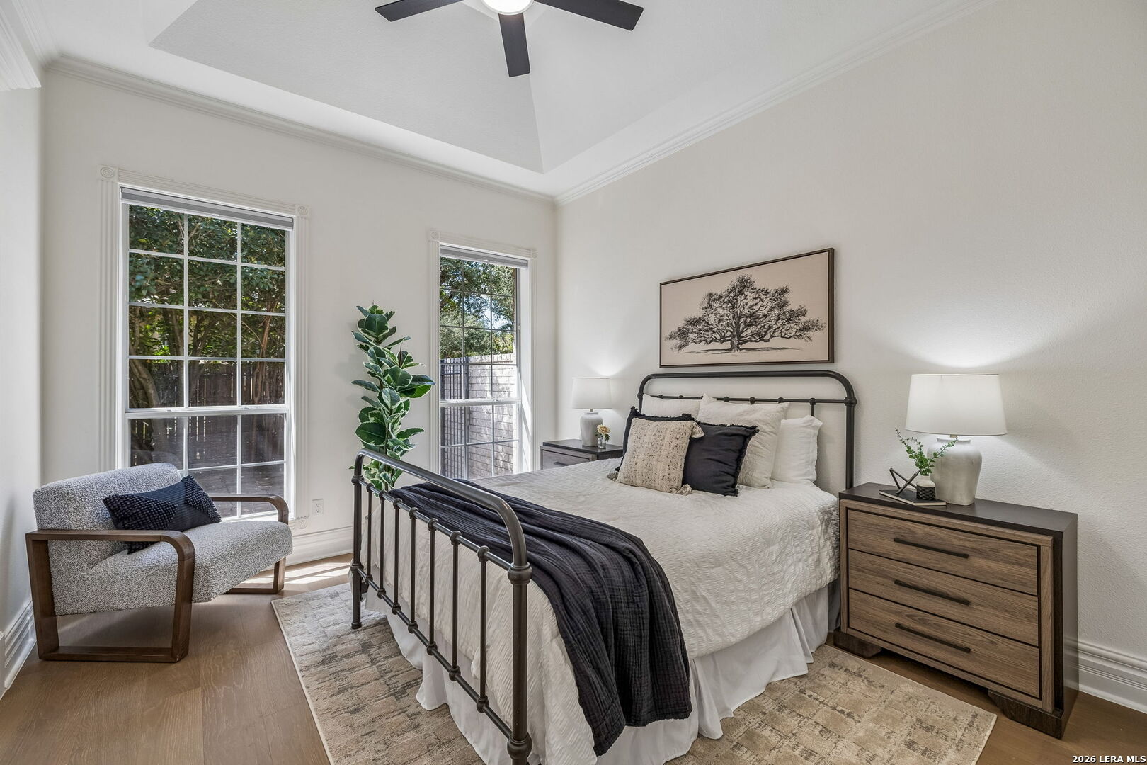 Staged bedroom with a black metal bed, vaulted ceiling, tall windows, and a gray armchair.