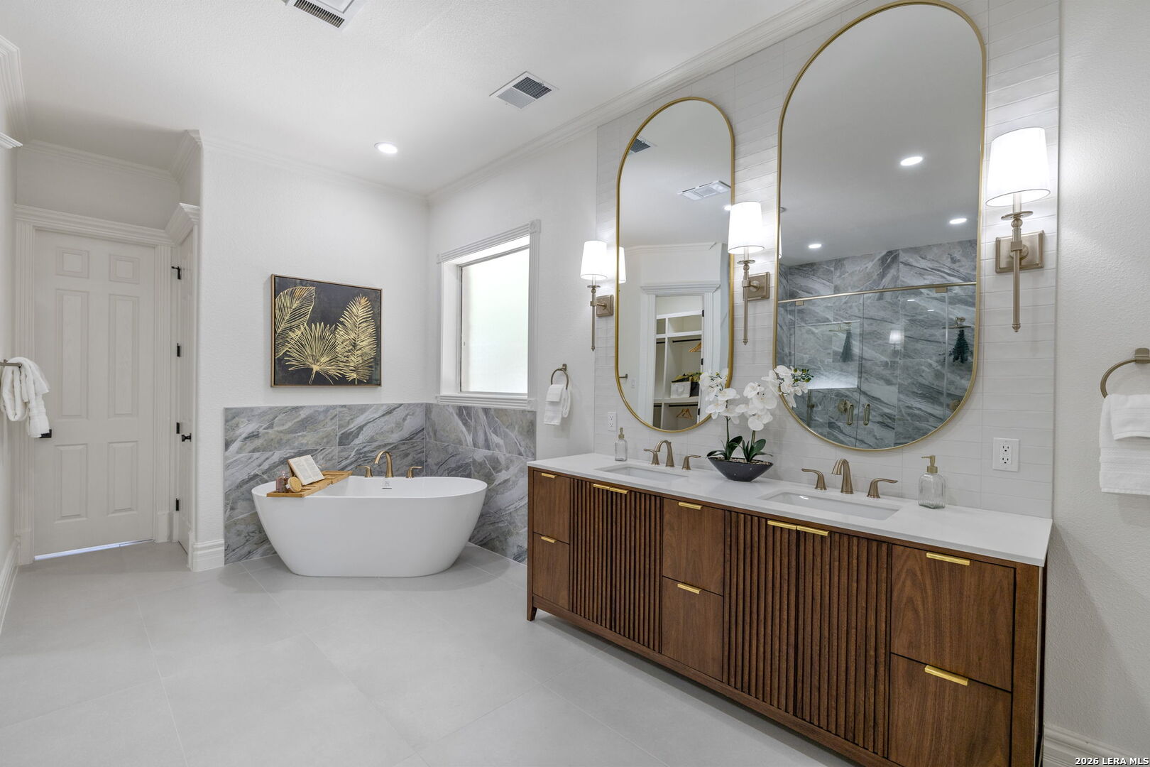 Bathroom with freestanding tub, marble-look tile, and a double wood vanity beneath arched mirrors.