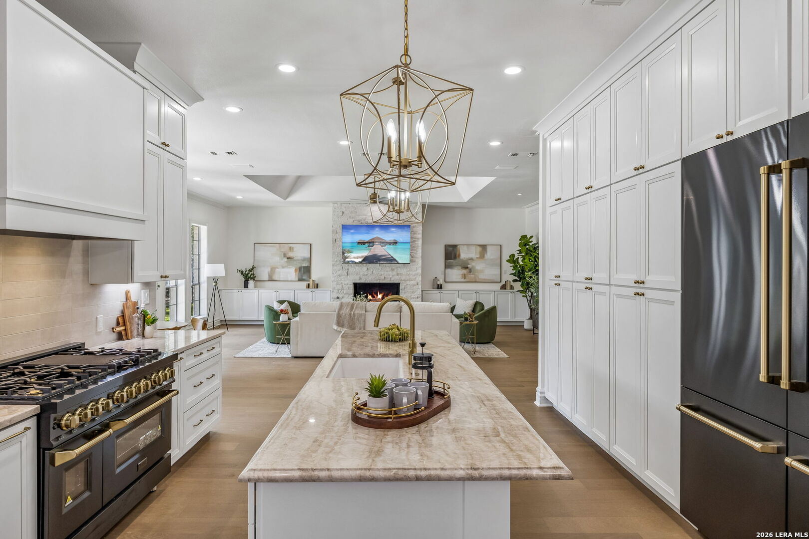 Open kitchen with a marble island, white cabinets, and a living room with a stone fireplace.