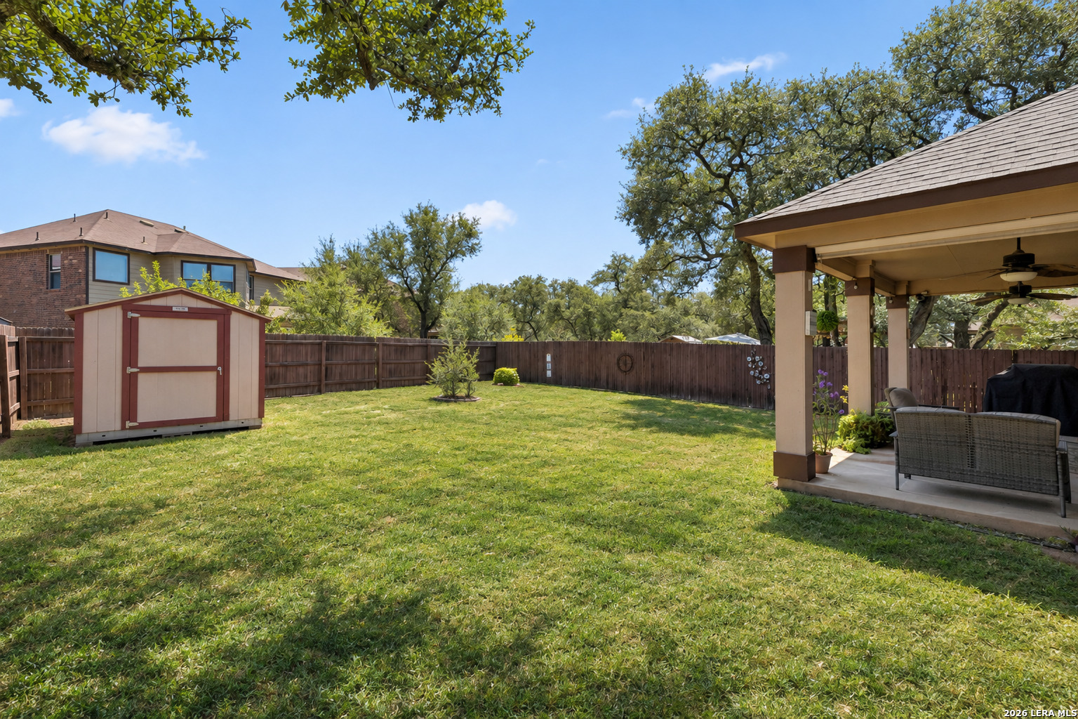 Fenced backyard with a broad lawn, storage shed, and covered patio with outdoor seating.
