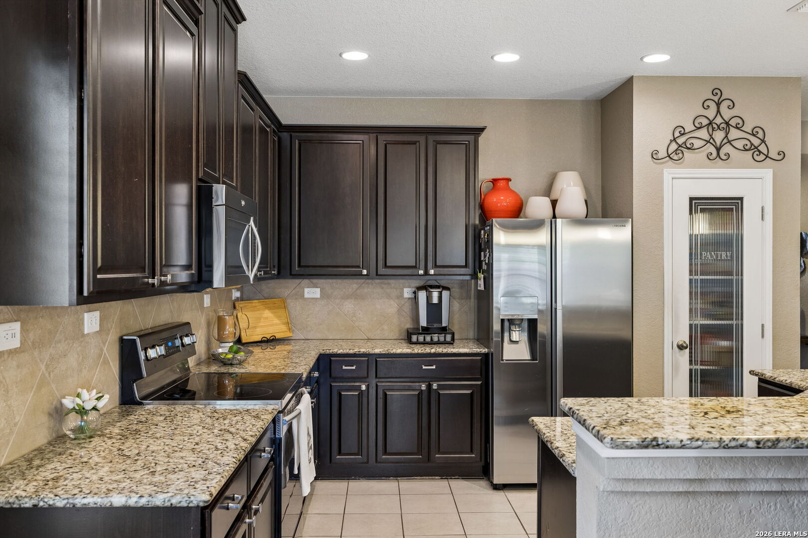 Kitchen with dark cabinets, granite counters, stainless appliances, and a glass-panel pantry door.