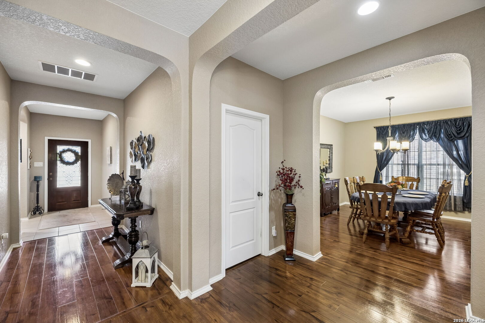 Entry hall opens through an archway to a furnished dining room with dark wood floors.
