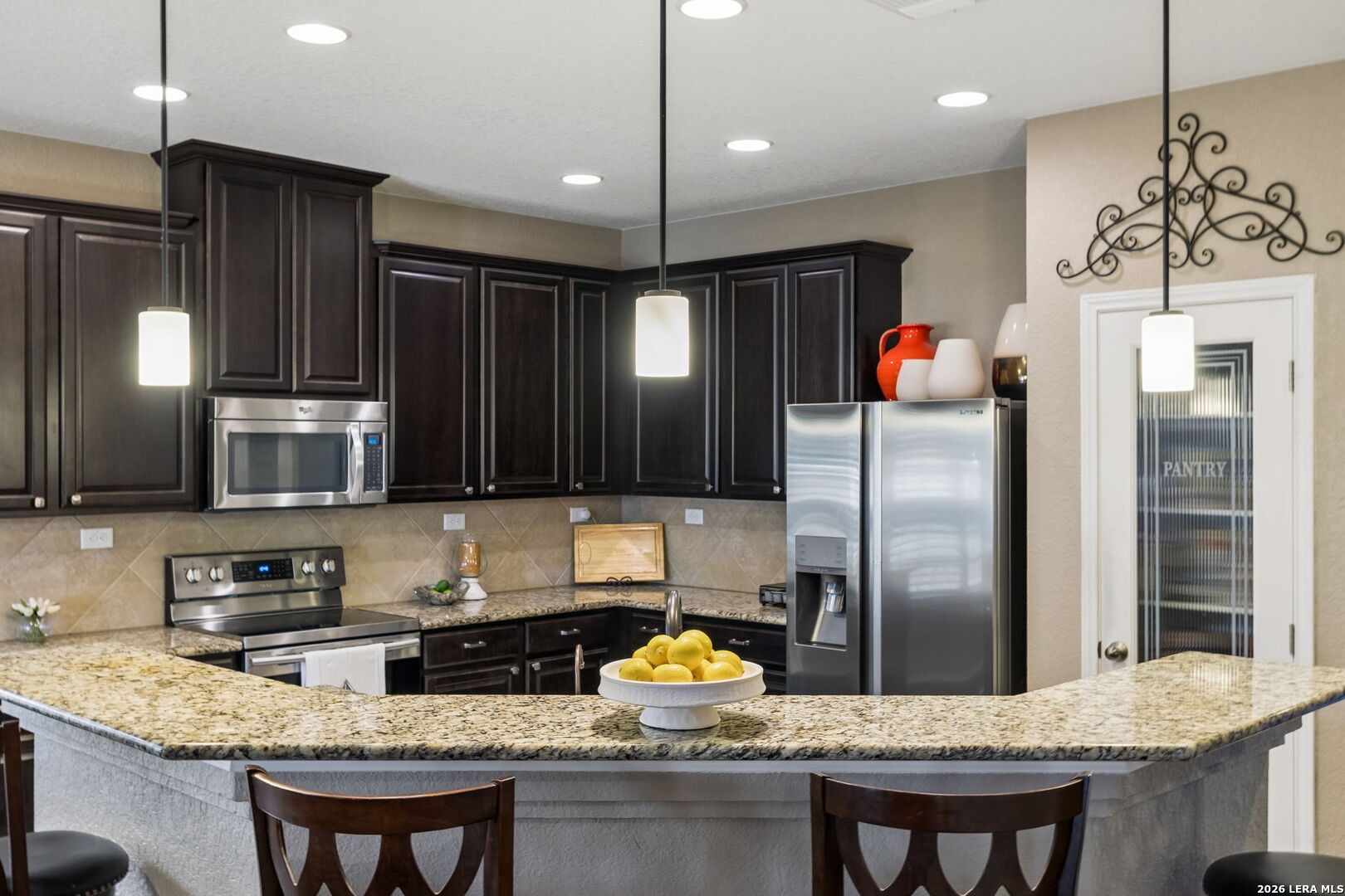 Kitchen with dark cabinets, stainless steel appliances, and a granite island topped with lemons.