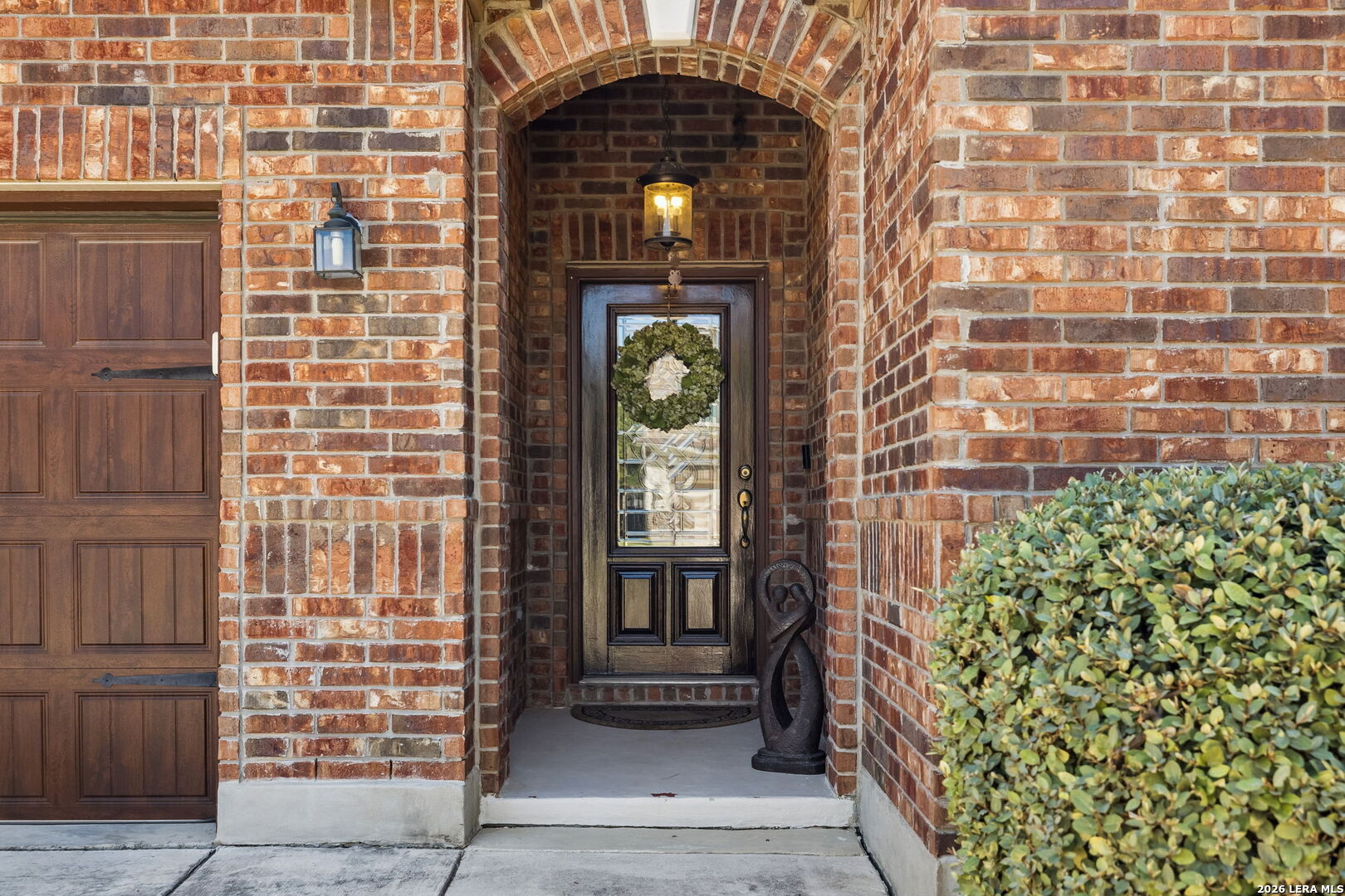 Brick home entrance with an arched porch and wreath on the glass-paneled front door.