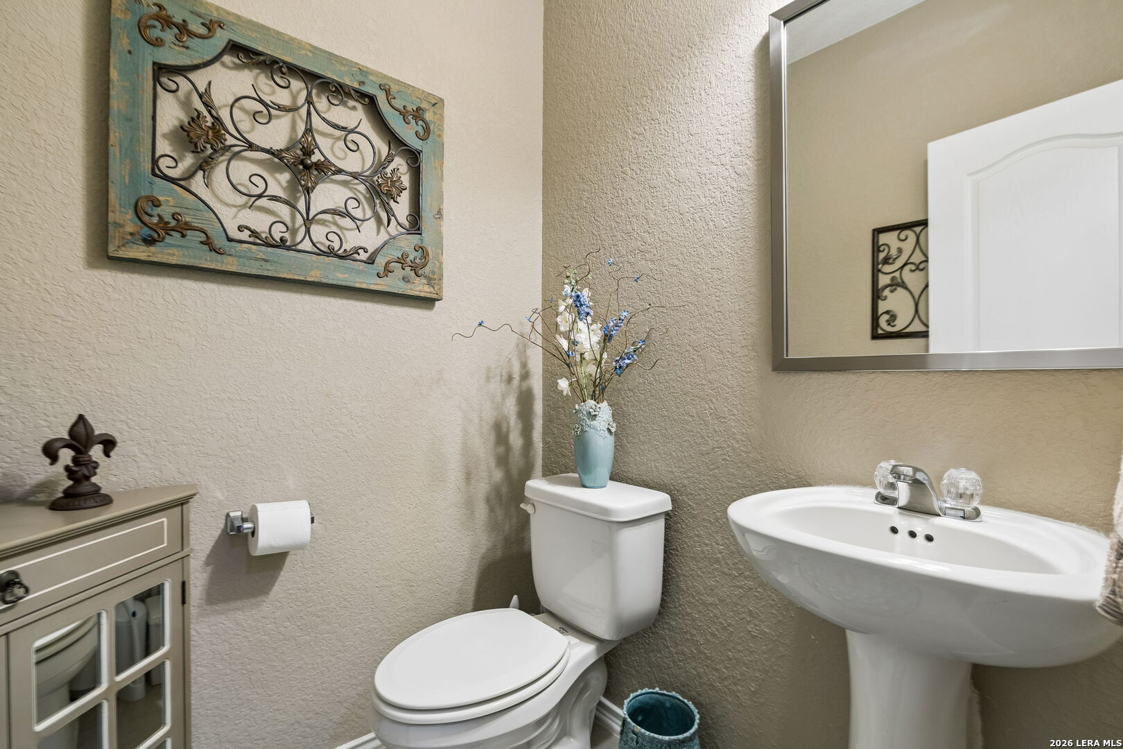 Bathroom with a white pedestal sink, toilet, large mirror, and ornate wall decor.