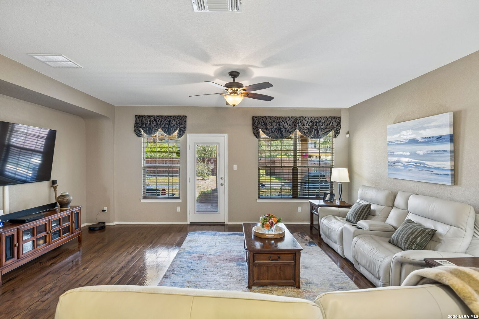Living room with a white sectional, dark wood floors, and a ceiling fan.