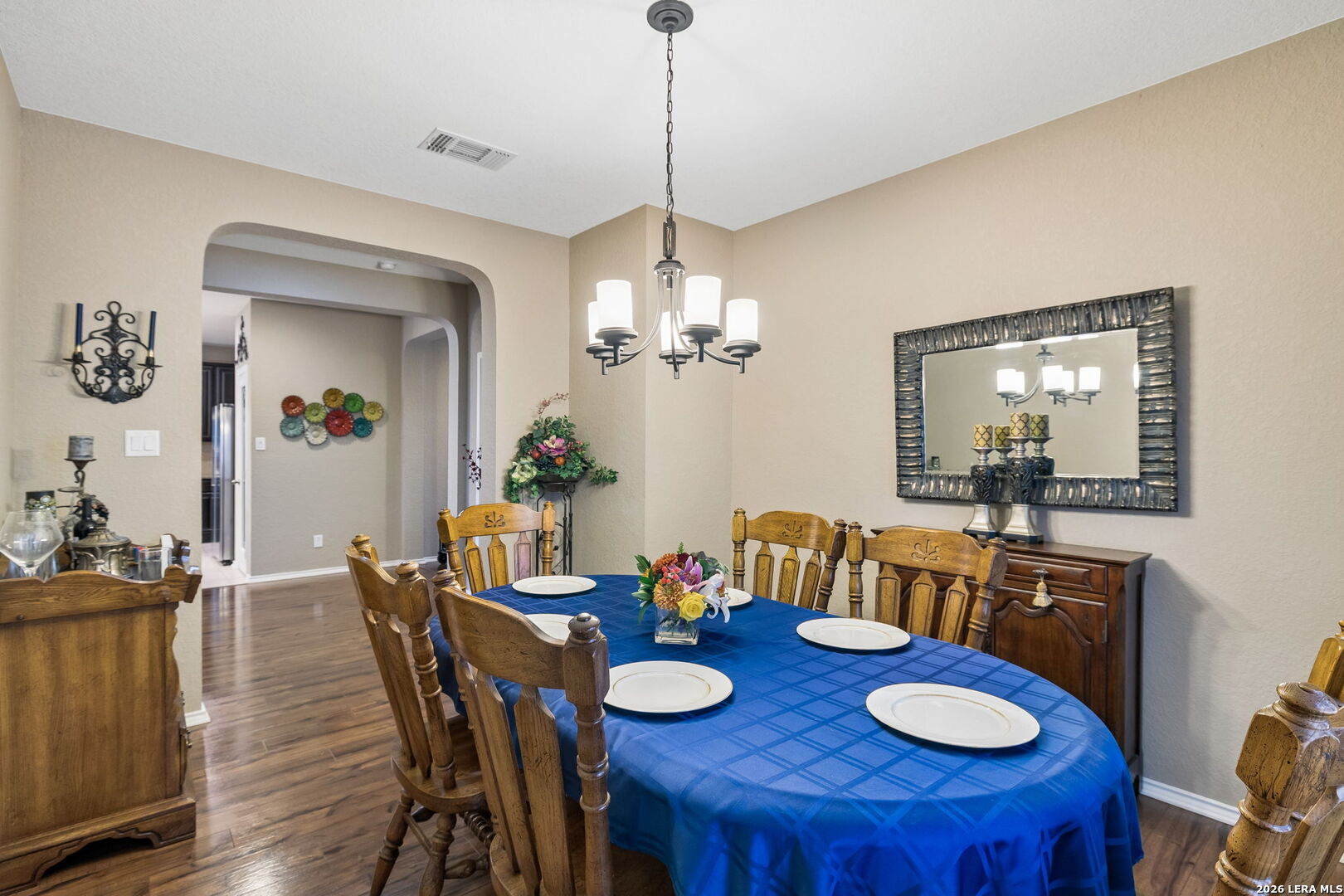 Dining room with a blue-covered table, wooden chairs, and a chandelier beneath an arched opening.