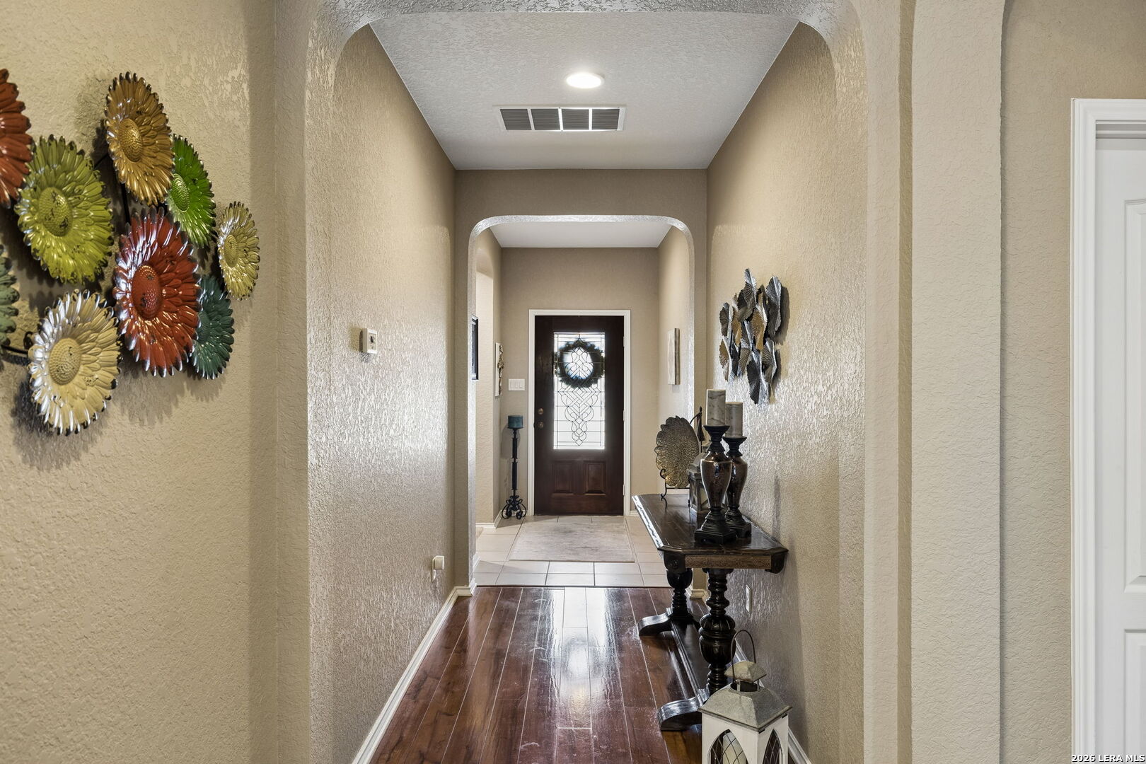 Entry hallway with arched openings, glossy wood floors, and a decorative glass-panel front door.