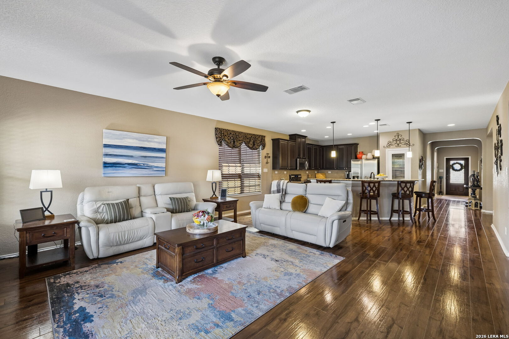 Furnished living room with white sofas, patterned rug, and open kitchen with a bar island.