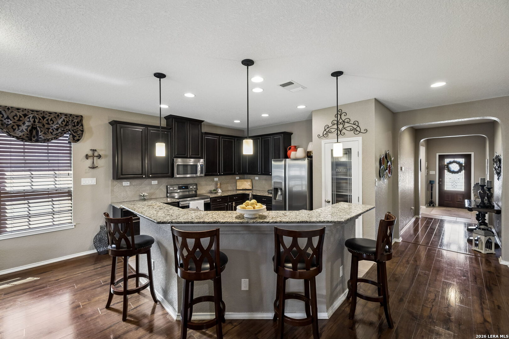 Kitchen with granite breakfast island, dark cabinets, stainless appliances, and wood flooring.