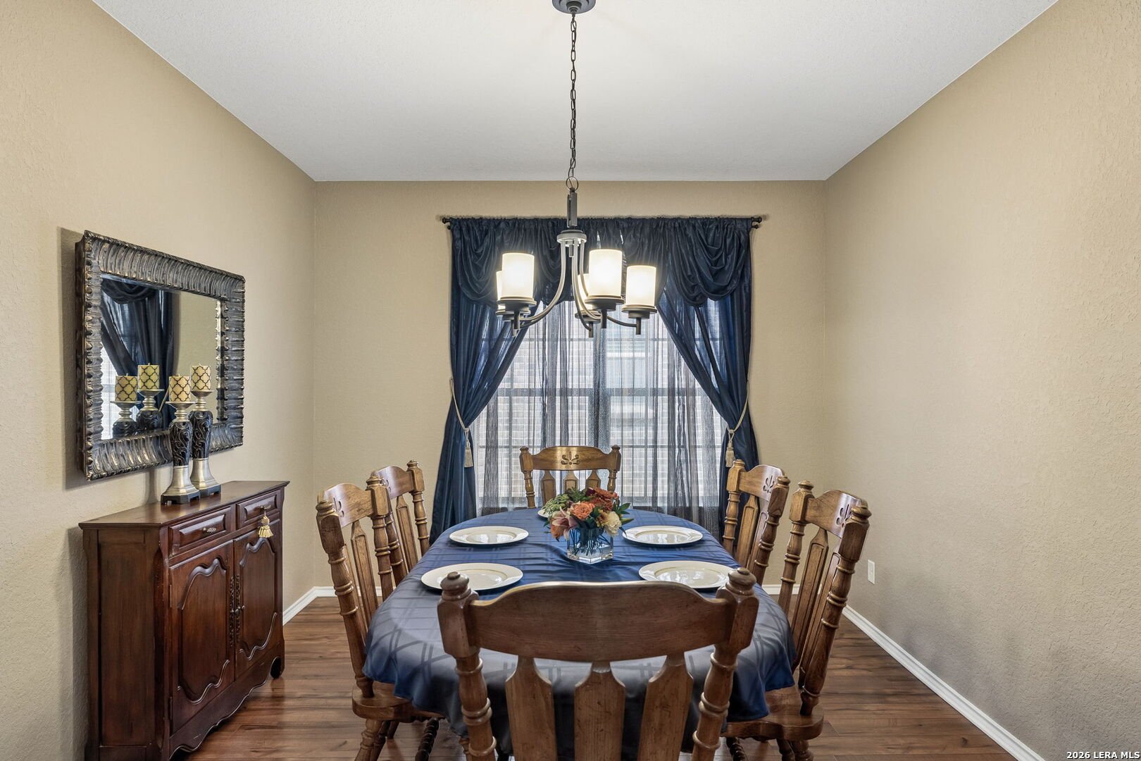 Dining room with a dark wood table, blue tablecloth, chandelier, and navy window curtains.