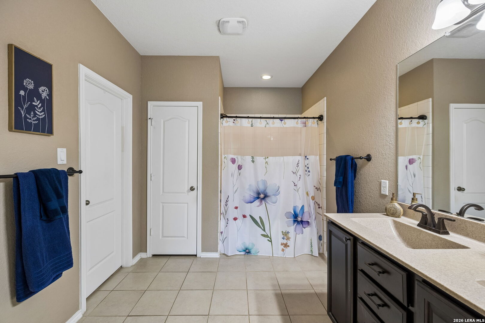 Bathroom with a double-sink vanity, large mirror, tiled floor, and floral shower curtain.