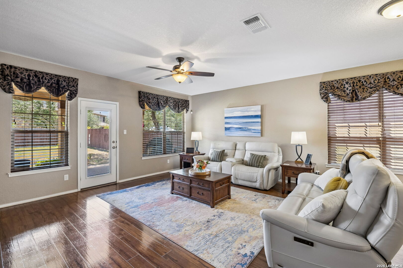 Furnished living room with white reclining sofas, dark wood floors, and a ceiling fan.