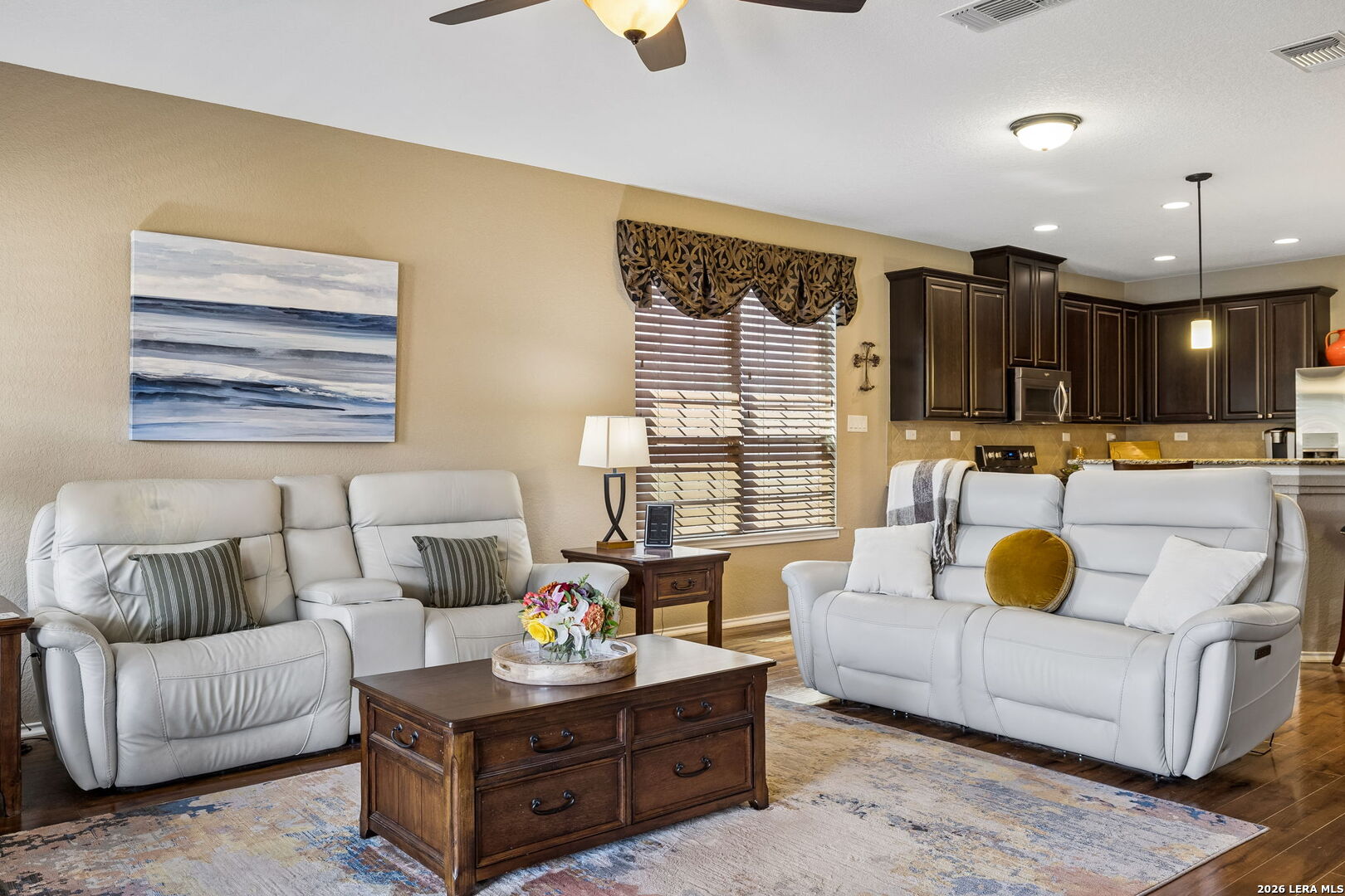 Living room with white leather sofas, a wooden coffee table, and dark kitchen cabinetry.